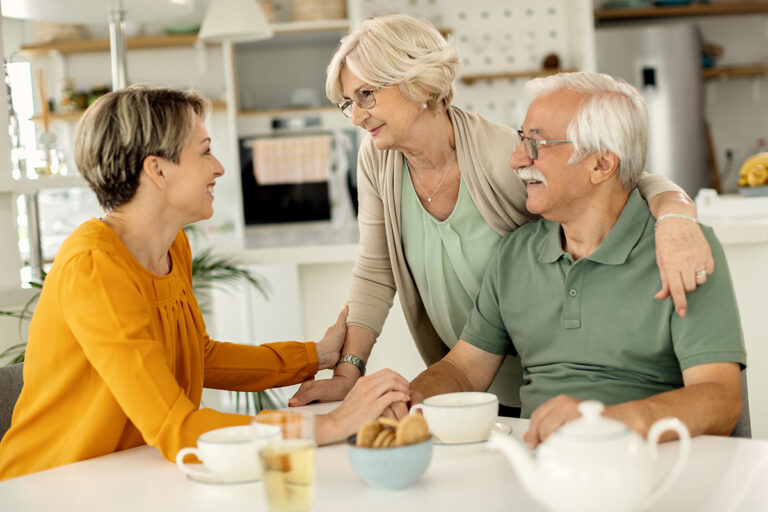 an elderley couple sat at a kitchen table conversing with a younger female