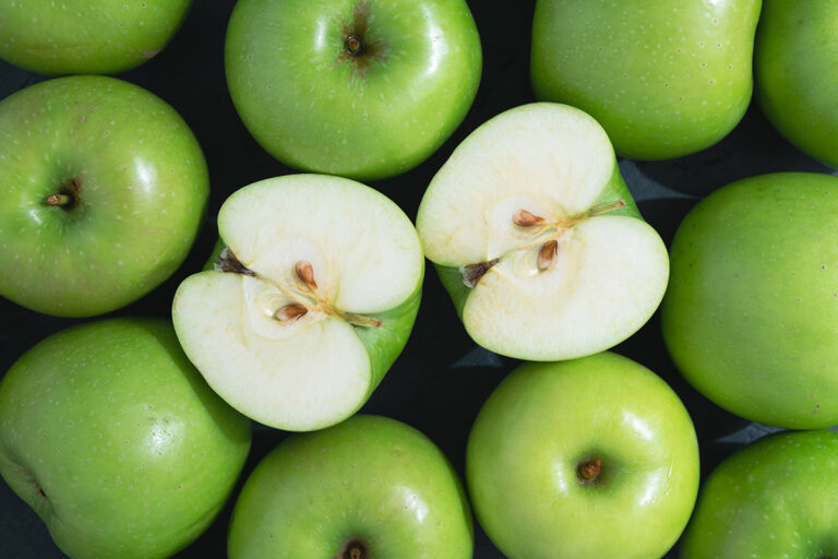 green apples piled up with one sliced open