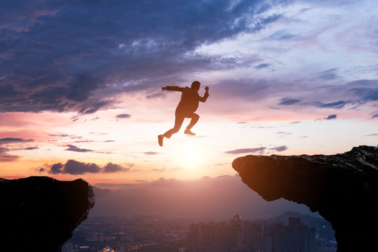 man in suit leaping across the two peices of mountain